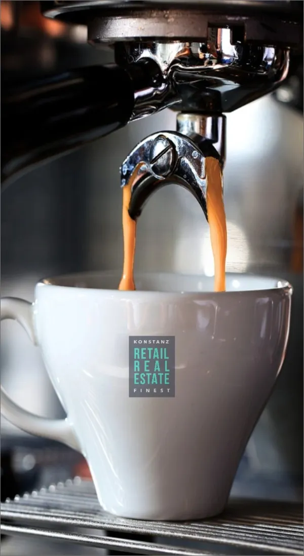 Frisch geröstete Kaffeebohnen werden in eine weiße Keramiktasse gegossen, welche das Logo von Konstanz Finest | Retail Real Estate abbildet.
